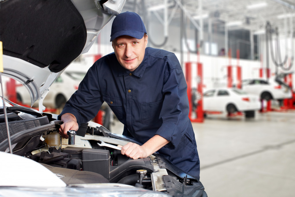 mechanic in blue uniform inspecting and working on a car